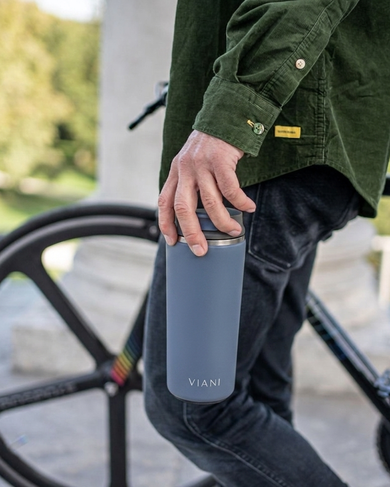 Vaso térmico MugsCafe VIANI azul en la mano, junto a una bicicleta